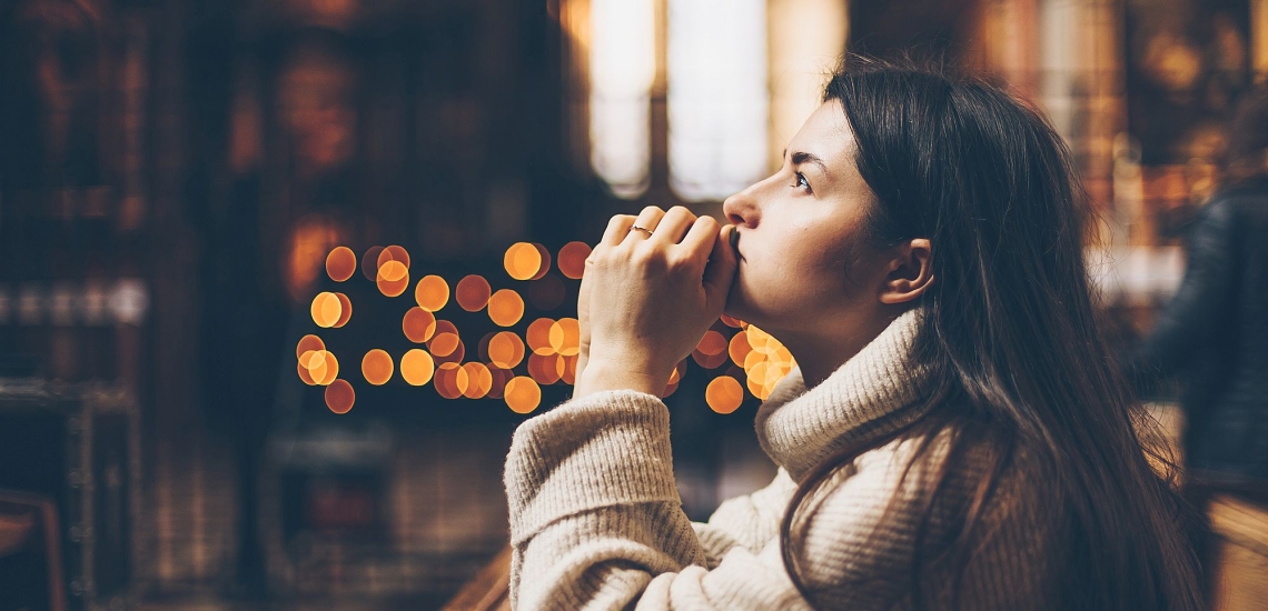 Junge Frau sitzt nachdenklich in einer Kirche, den Blick nach oben gerichtet