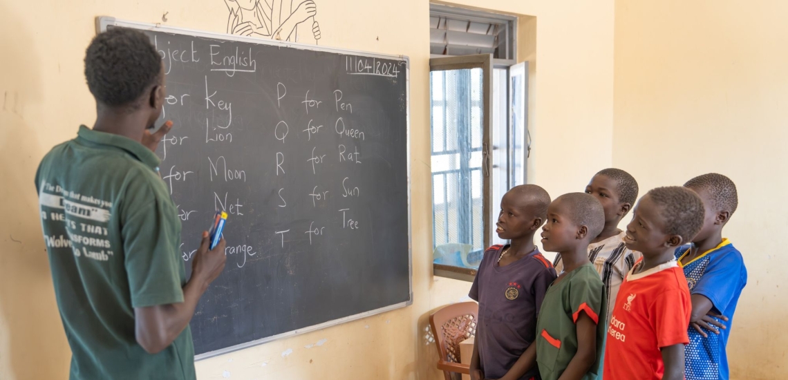 Lehrer und Schülergruppe in Klassenzimmer vor Tafel mit Aufschrift Subject English