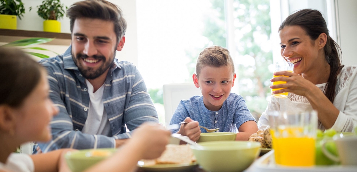 Vater, Mutter und zwei Kinder sitzen lachend am gemütlichen Frühstückstisch
