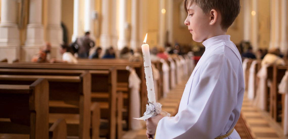 Erstkommunion - Junge mit Kerze im Mittelgang einer Kirche