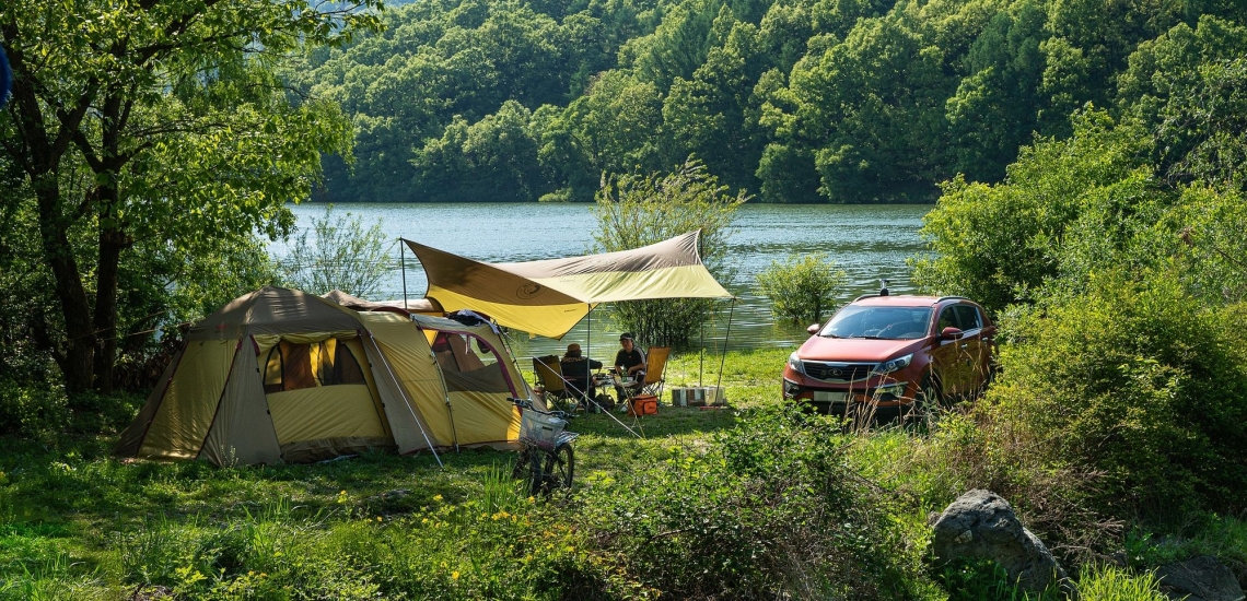 Zelt mit Vordach und Auto in der Natur an einem See bei Sonnenschein