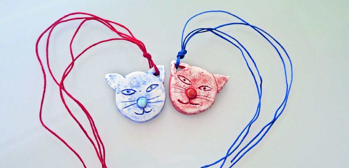 zwei Anhänger in Form von Katzenköpfen, bemalt mit roter und blauer Farbe