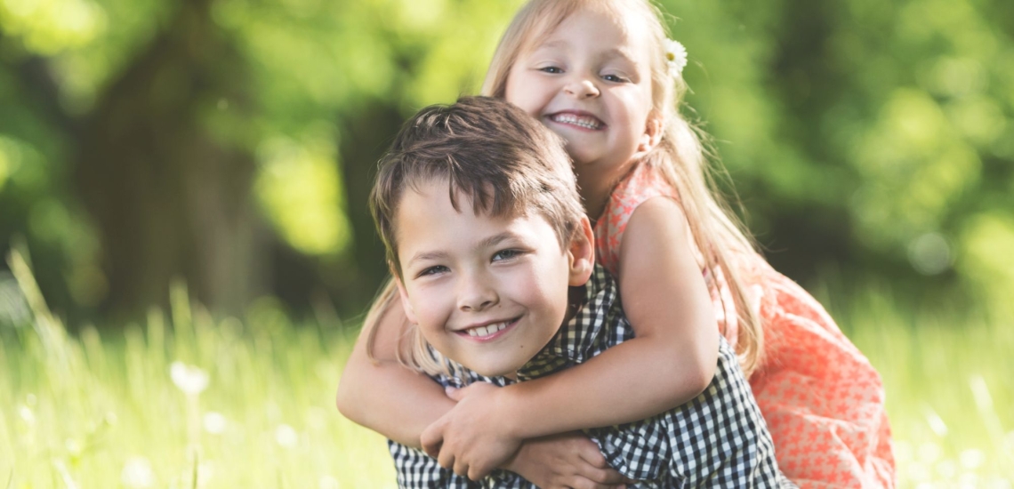 Zwei Kinder lachend im Grünen, Junge trägt Mädchen auf dem Rücken