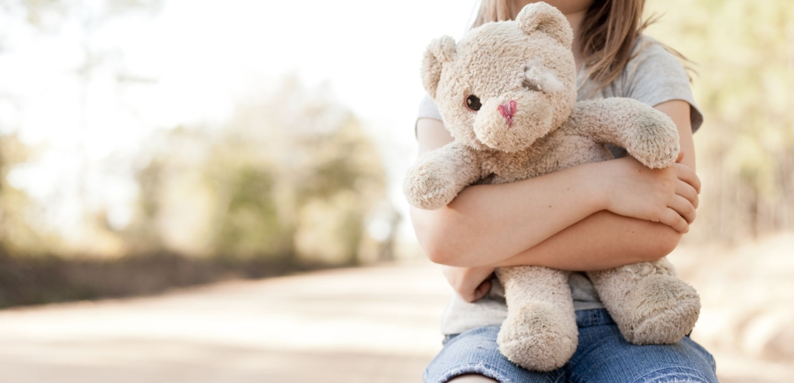 Teddy mit abgenutztem Fell und nur einem Auge in Arm von Kind