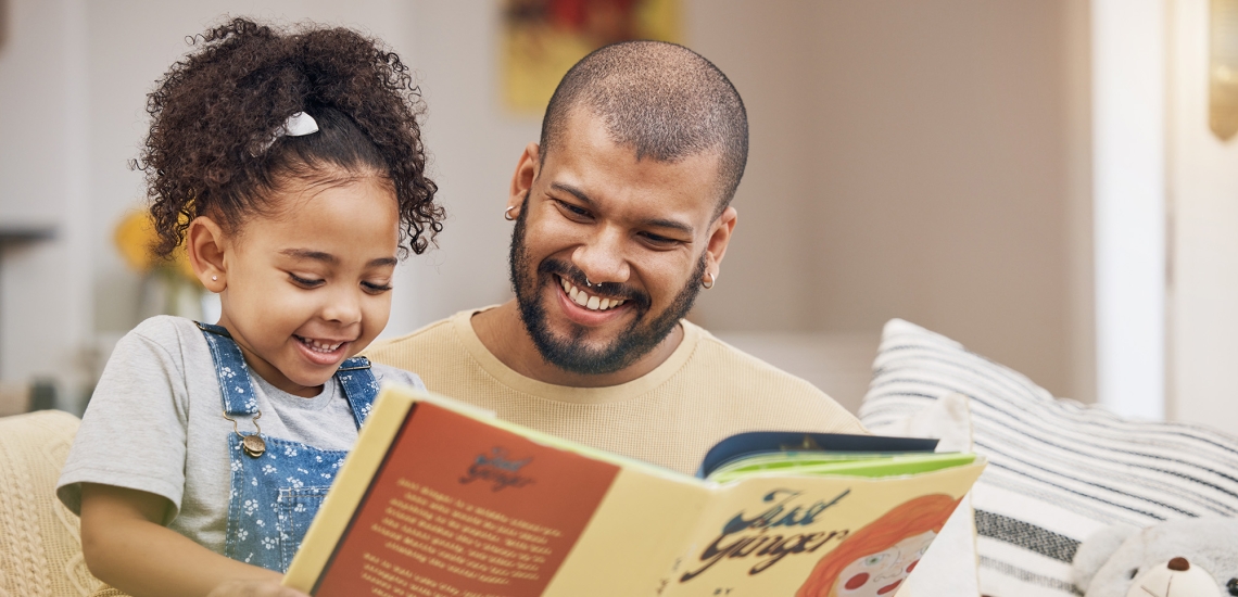 Ein Vater sitzt mit seiner kleinen Tochter auf der Couch und liest ihr aus einem Buch vor