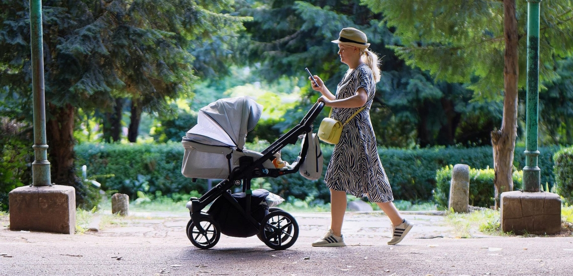 Mutter schiebt Kinderwagen durch Park