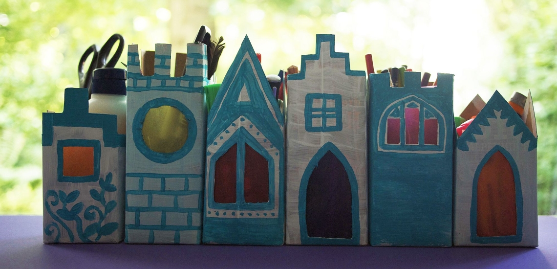 Aus Tetrapaks gebastelte Lichterhäuschen, in denen Stifte und eine Schere zur Aufbewahrung stecken