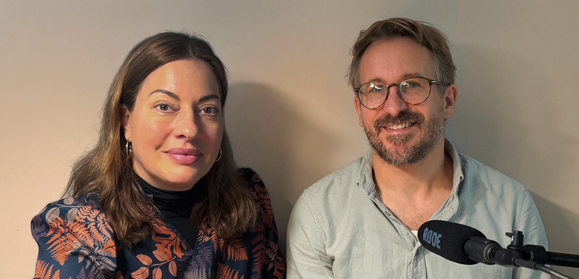 Julia Dahmen und Christian Pröls-Geiger lächeln in die Kamera. Am unteren rechten Bildrand ist ein Mikrofon zu sehen.
