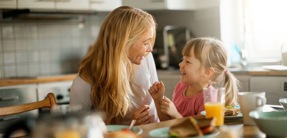 Mutter und kleine Tochter scherzen beim Frühstück in einer gemütlichen Küche