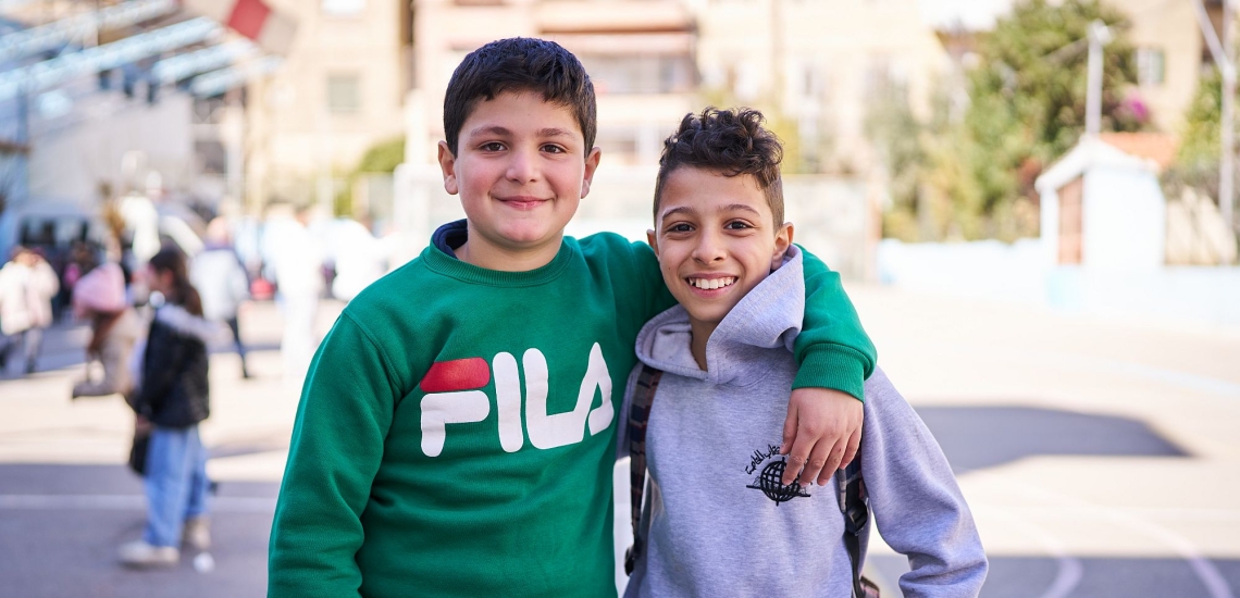 zwei Jungen lachen mit umeinander gelegten Armen in die Kamera