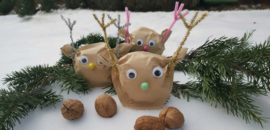 Rentiergesichter aus Filtertüten mit aufgeklebten Wackelaugen, daneben Tannenzweige und Walnüsse