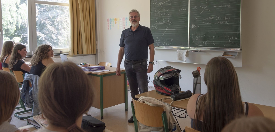 Lehrer steht vor Tafel in Klassenzimmer mit Schülerinnen