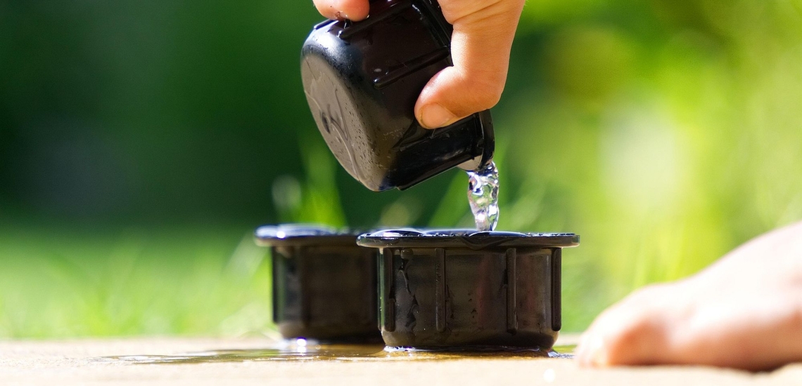 Kinderhand schüttet Wasser aus einem Becher in einen anderen