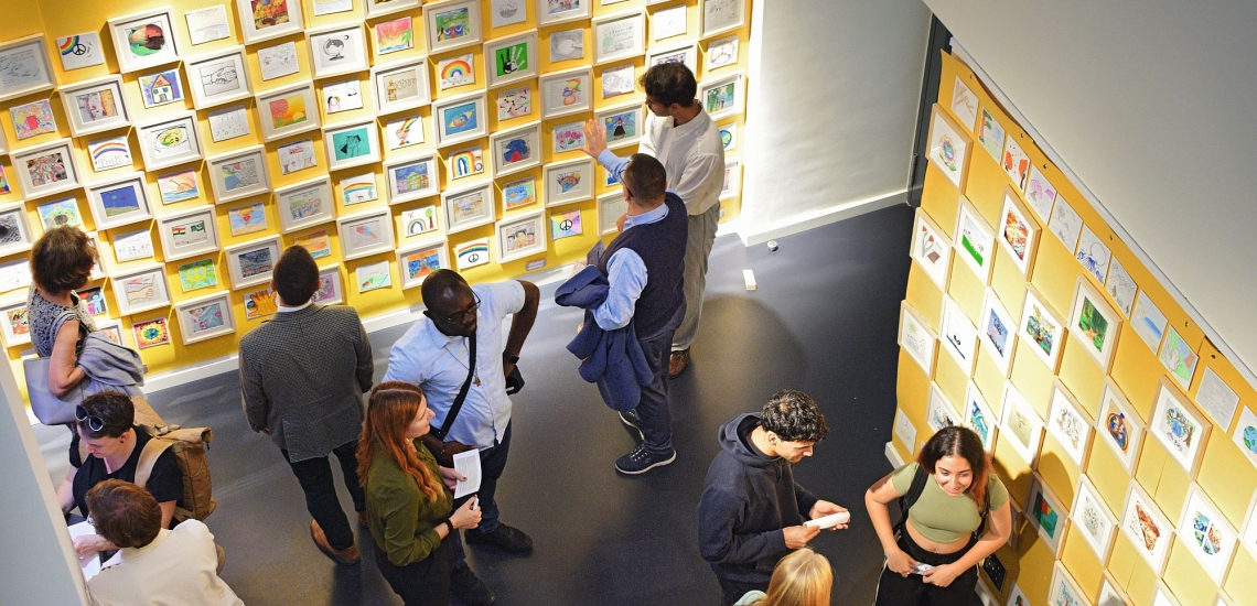 Menschen in Ausstellungsraum betrachten Kunstwerke von Kindern und Jugendlichen