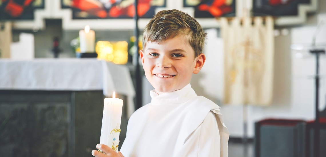 Erstkommunionkind mit Kerze in Kirche vor Altar