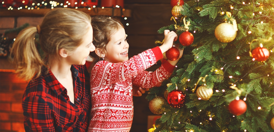 Ein Mädchen schmückt zusammen mit seiner Mutter einen Christbaum
