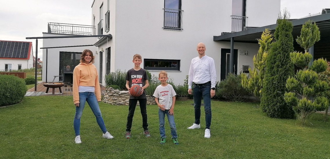 Vater, Mutter und zwei Kinder lachend vor großem Haus im Garten