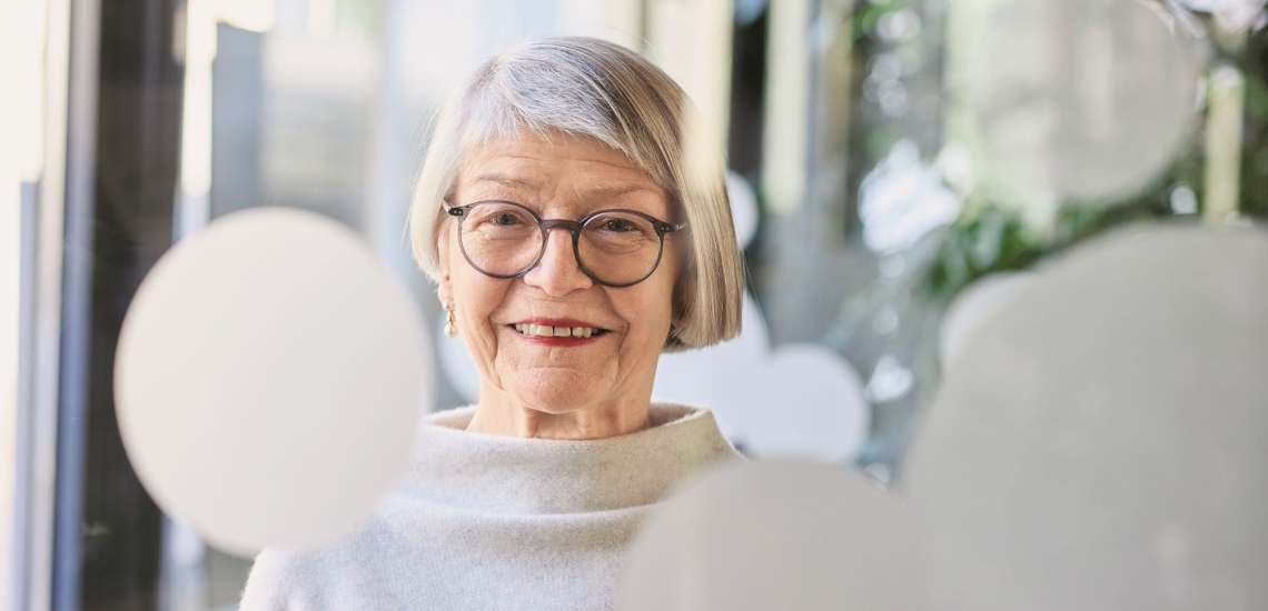 Frau mit moderner Frisur, Brille und Ohrringen vor Glastür mit halbtransparenten weißen Kreisen