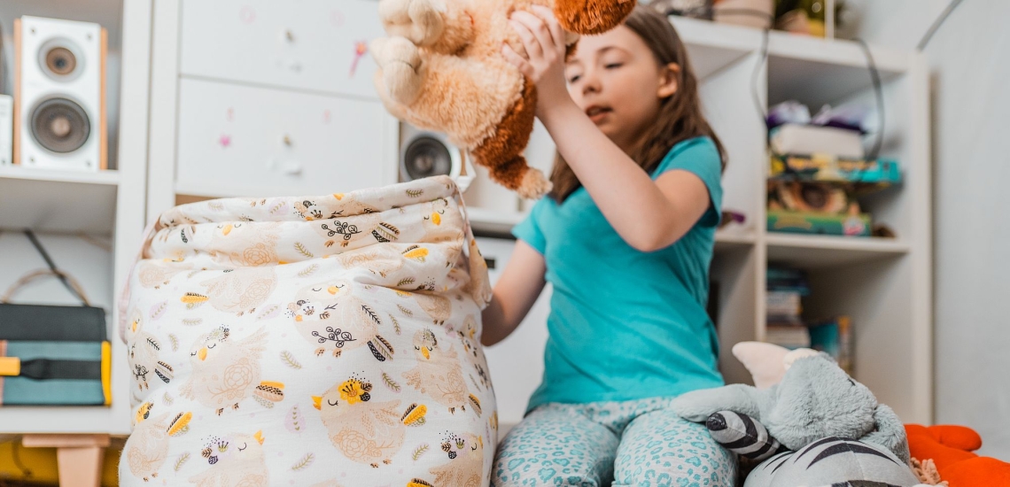 Kind räumt Kuscheltiere in einen Stoffsack, dahinter volle Regale