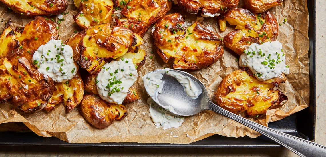 Smashed Potatoes auf einem Blech mit Schnittlauch-Dip und Löffel