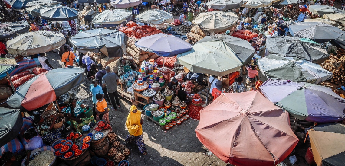 Markt mit Schirmen über den Waren und durch die Gassen laufenden Menschen