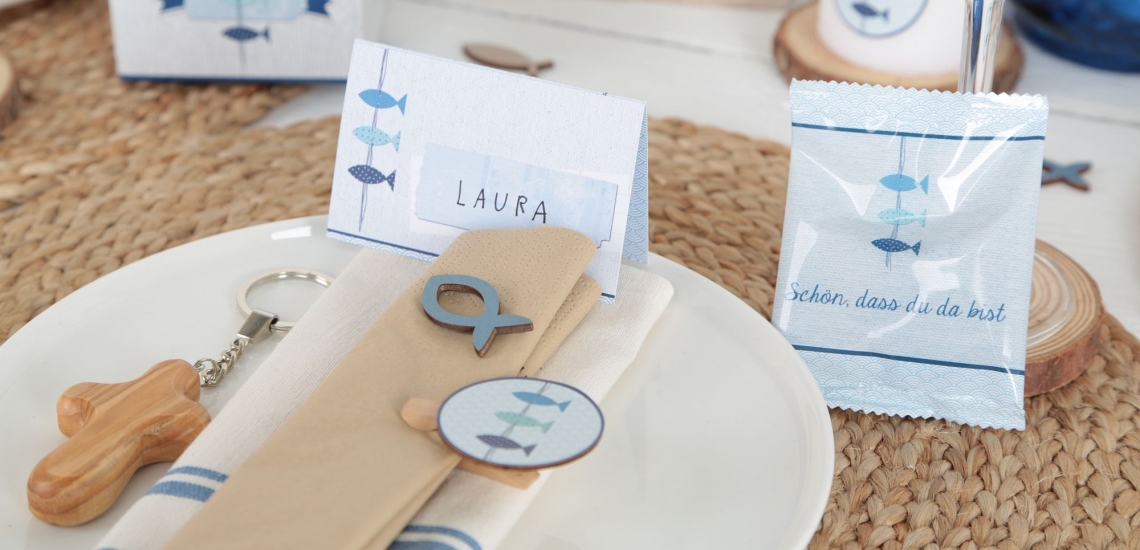 festlich gedeckter Tisch für die Feier der Firmung mit kleinem Holzkreuz sowie Tischkarten und Servietten mit Fisch-Motiv