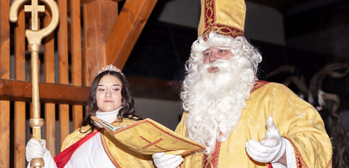 Als Bischof Nikolaus kostümierter Mann liest aus goldenem Buch, daneben eine Frau im Engelskostüm, die den Bischofsstab hält