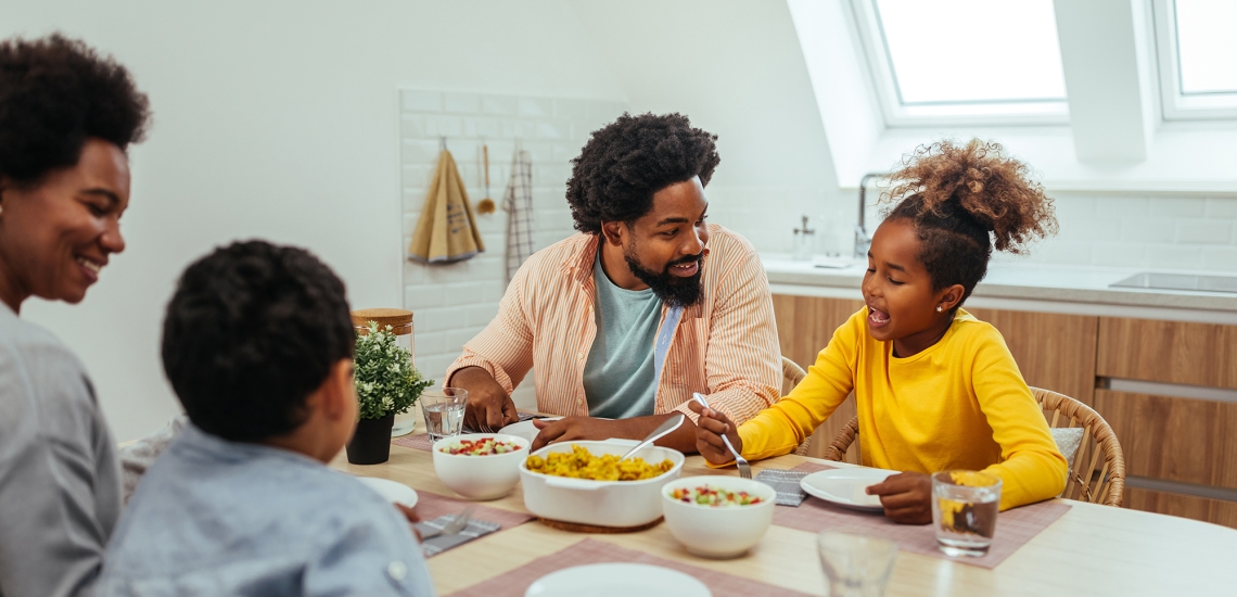 Eine Familie sitzt zusammen am Küchentisch, unterhält sich und isst.