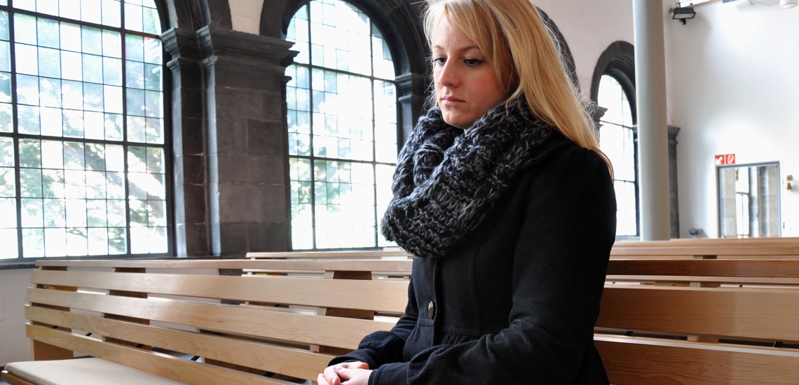 Junge Frau sitzt mit nachdenklichem Blick in Kirchenbank
