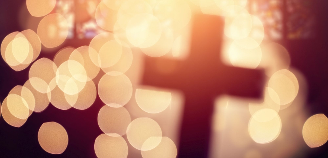 Abstraktes Kreuz in einer Kirche, umgeben von hellgelben Lichtpunkten