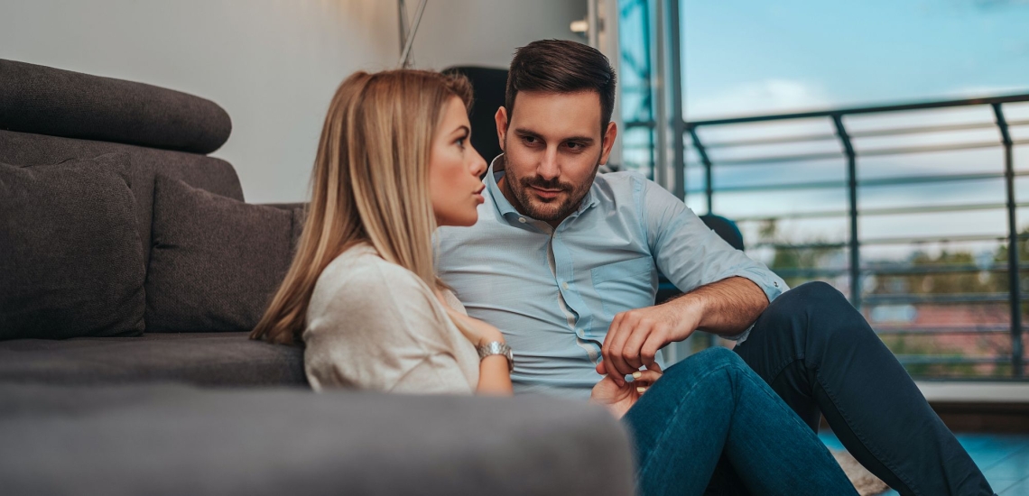 Junges Paar sitzt auf Boden vor Couch und spricht intensiv miteinander