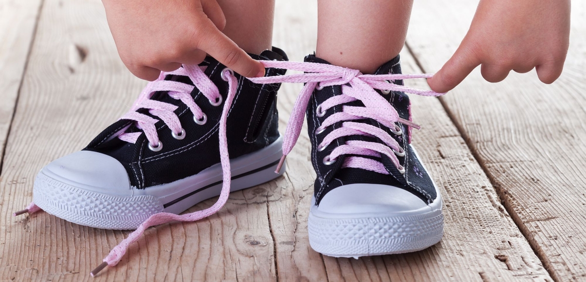 Kind bindet Schleife mit rosa Schnürsenkeln an dunkelblauen Turnschuhen