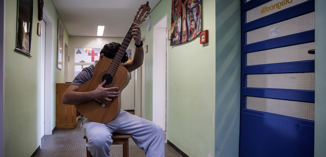 Jugendlicher Häftling mit Gitarre vor dem Gesicht in einem Gang