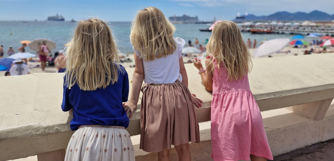 Drei blonde Mädchen blicken aufs Meer - Rückensansicht