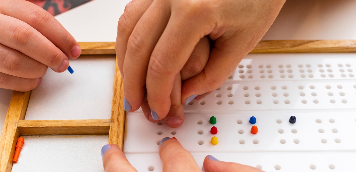 Hände eines Erwachsenen führen Kinderhände über ein Brailleboard
