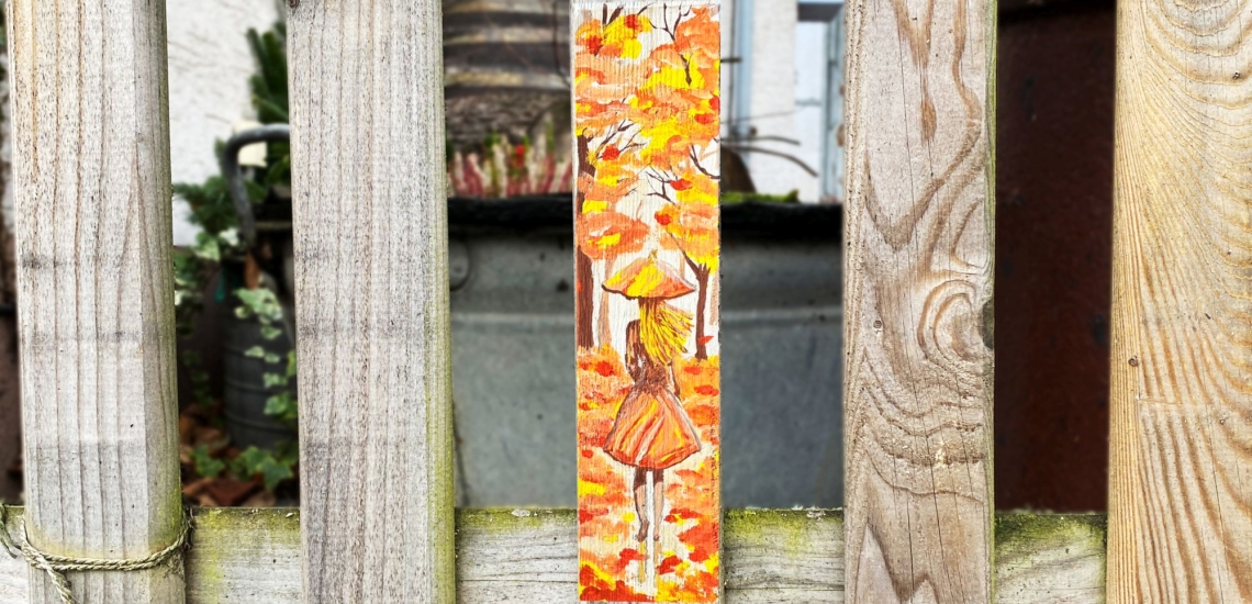 Bemalte Zaunlatte an einem Holzzaun zeigt eine Frau in Herbstwald