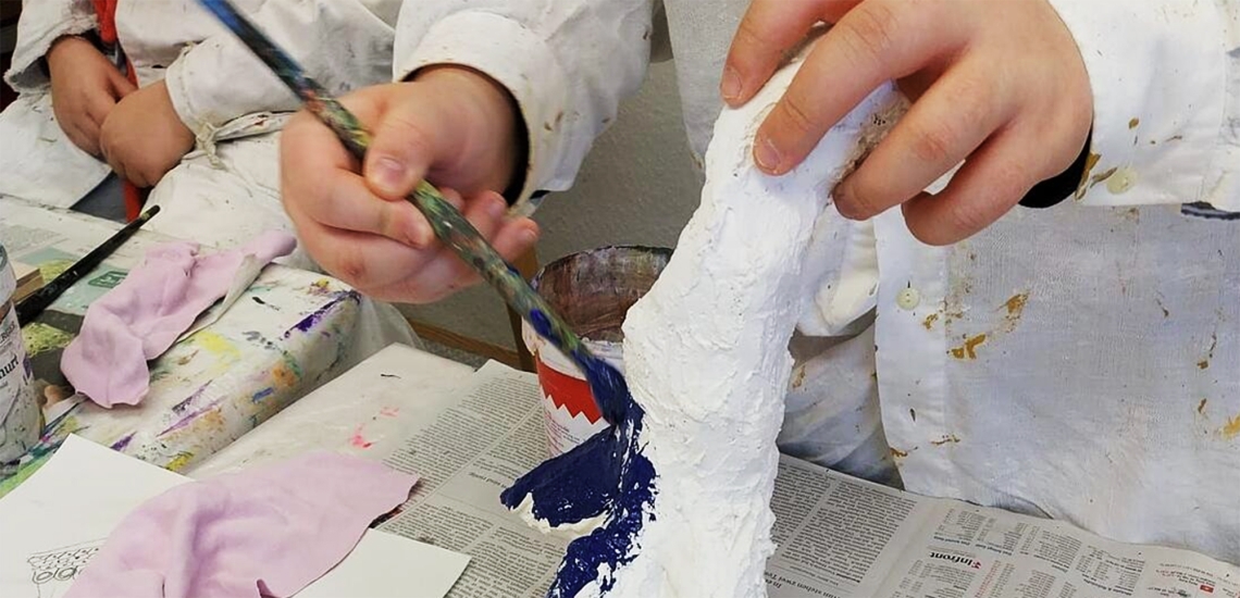 Junge Hände, die eine Gipsskulptur halten und mit dunkelblauer Farbe bepinseln.