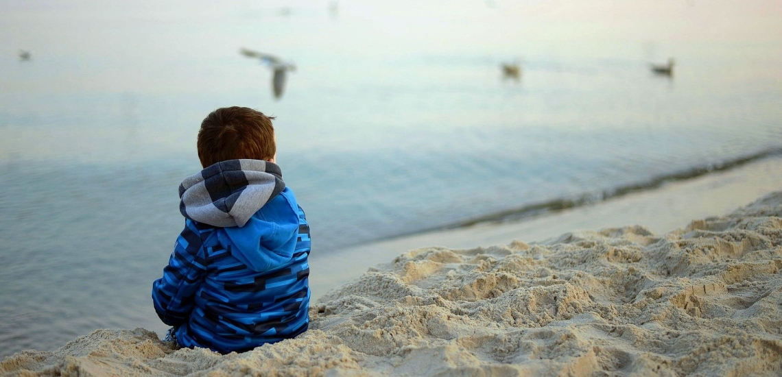 Kind sitzt einsam an Strand 