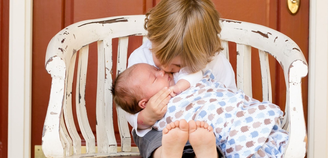 Kind küsst Baby das auf seinem Schoß liegt