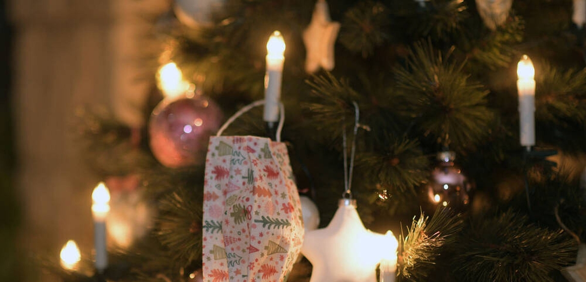 Maske hängt an beleuchtetem Weihnachtsbaum 