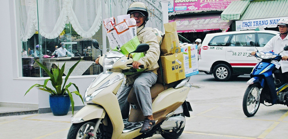 Francis van Hoi auf mit Einkäufen beladenem Roller