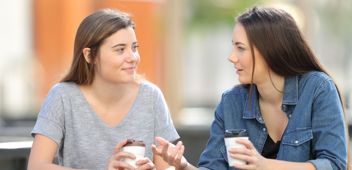 zwei Schwestern unterhalten sich draußen und trinken Kaffee