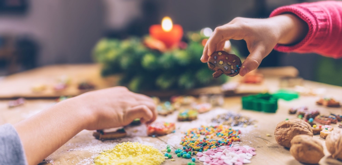 Kinderhände mit Keksen und Dekoration, im Hintergrund ein Adventskranz 