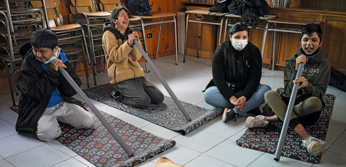 Junge Menschen sitzen im Kreis und halten große Metallrohre zum Hineinblasen in den Händen