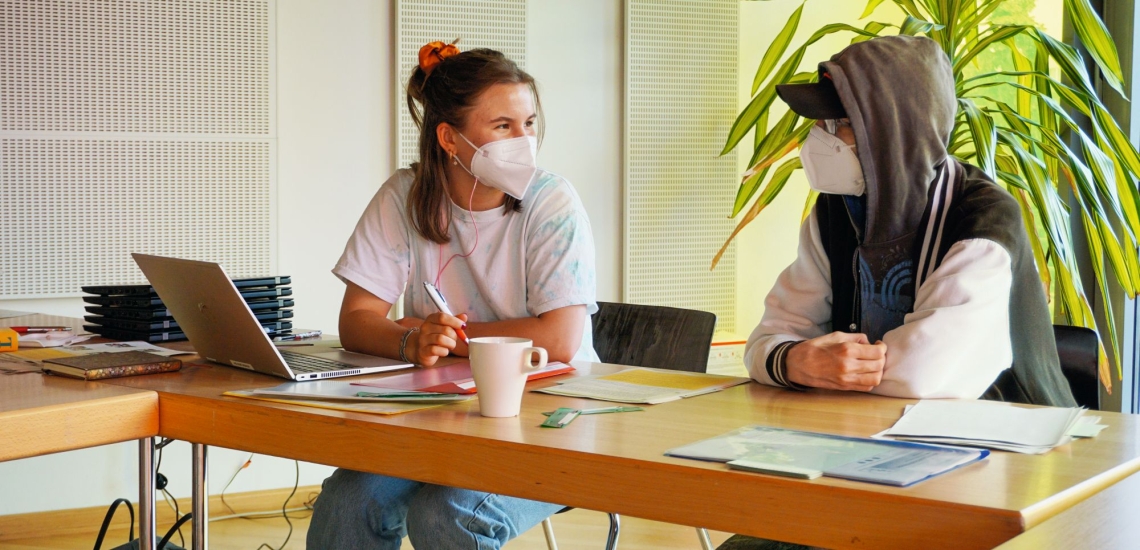 Betreuerin und junger Mensch sitzen an Schreibtisch beim Gespräch 