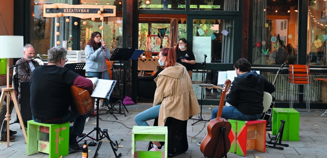 Band vor Gebäude, junge Frau am Mikrofon singt 