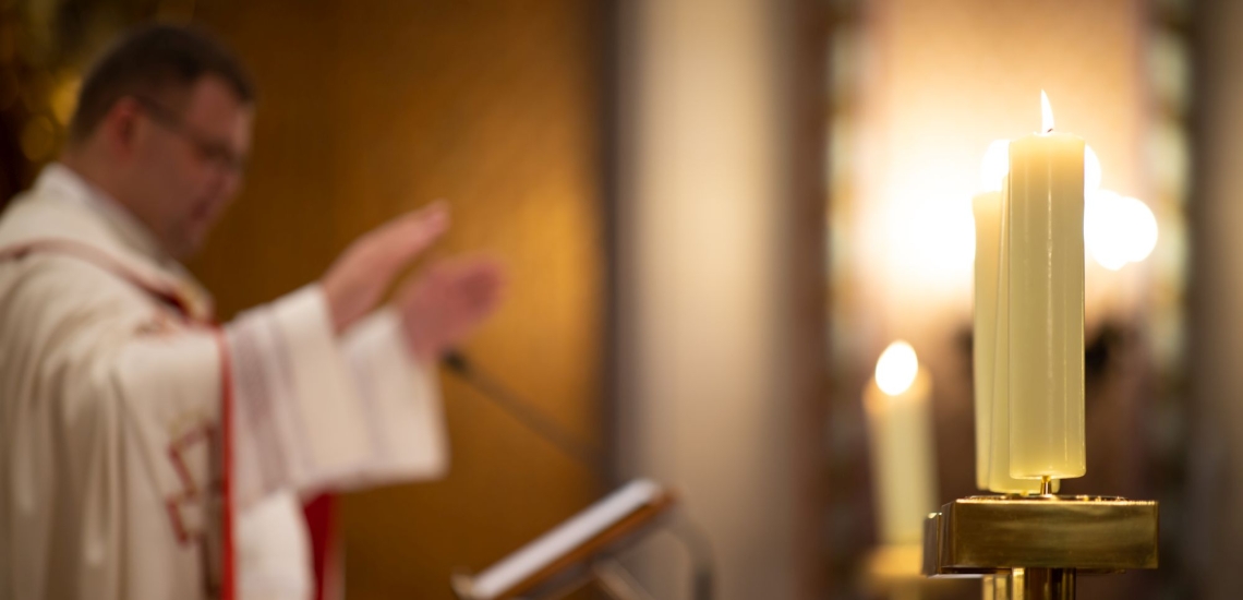 Priester mit ausbebreiteten Armen am Ambo in Kirche 