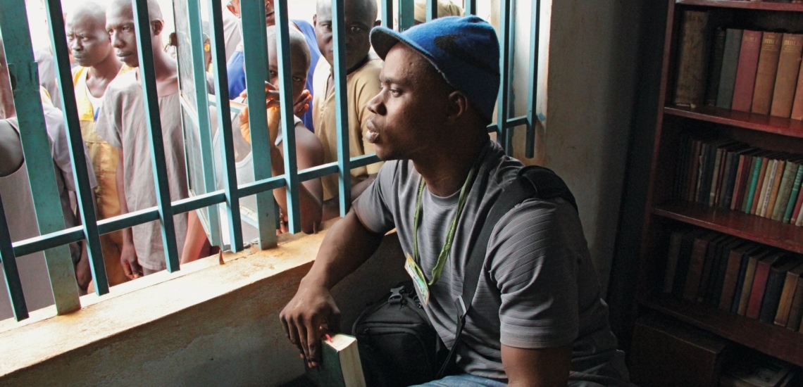 Junger Mann schaut durch Gitter zu anderen Menschen 