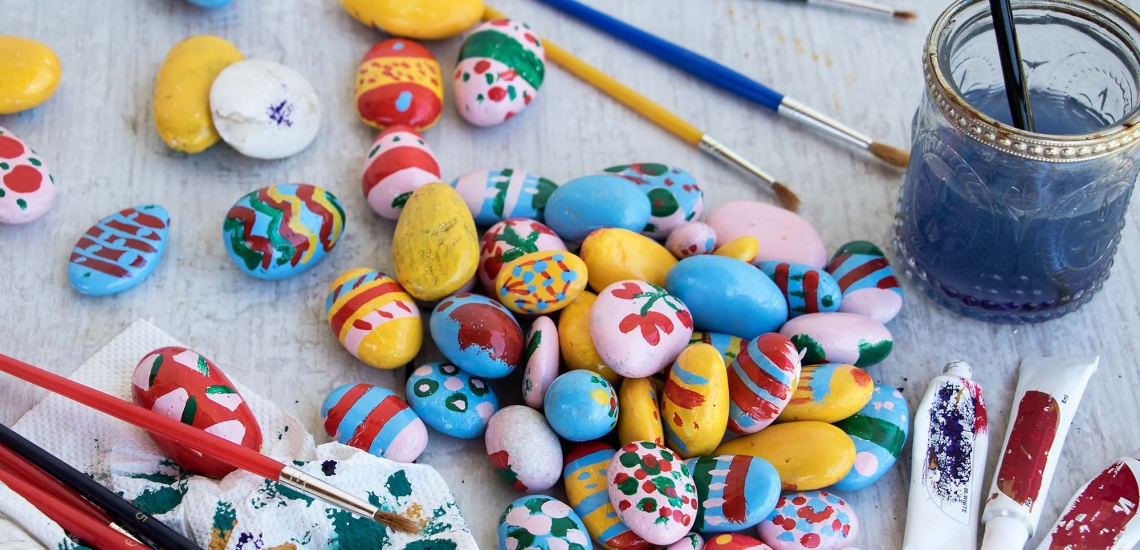 bunt bemalte Steine mit Pinseln und Farbe auf einem Basteltisch