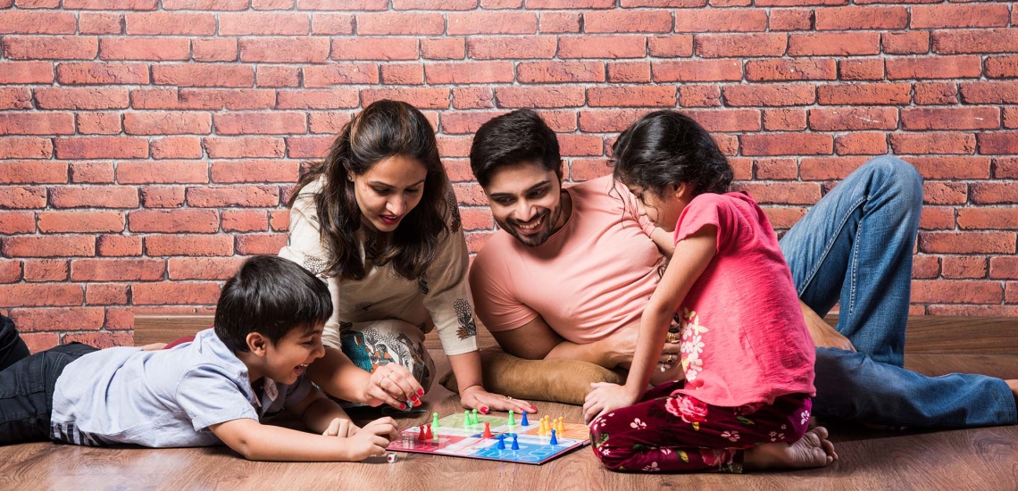 eine Familie mit zwei Kindern sitzt auf dem Boden und spielt ein Brettspiel